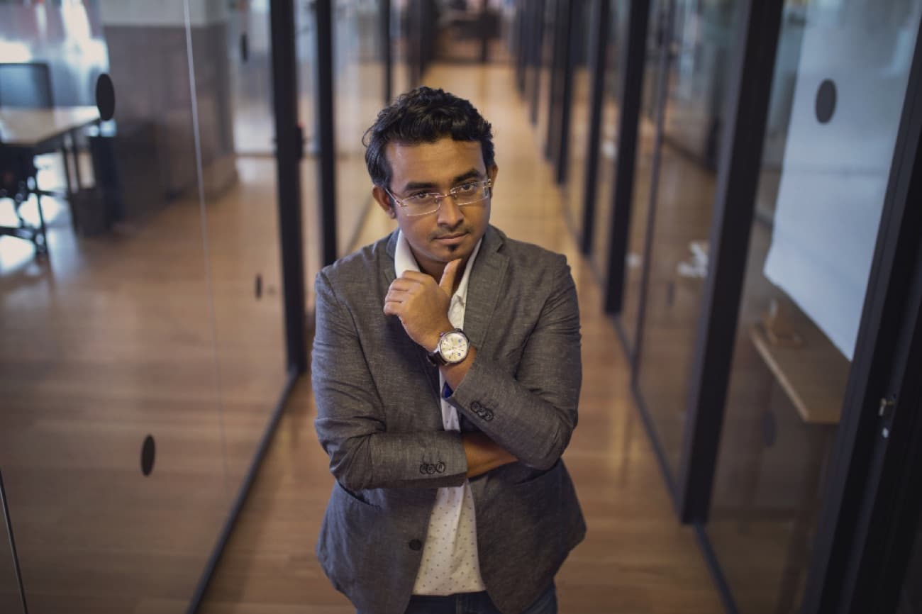 Daniel Mensah, a confident advisor in a gray blazer and glasses, in a modern glass-walled office
